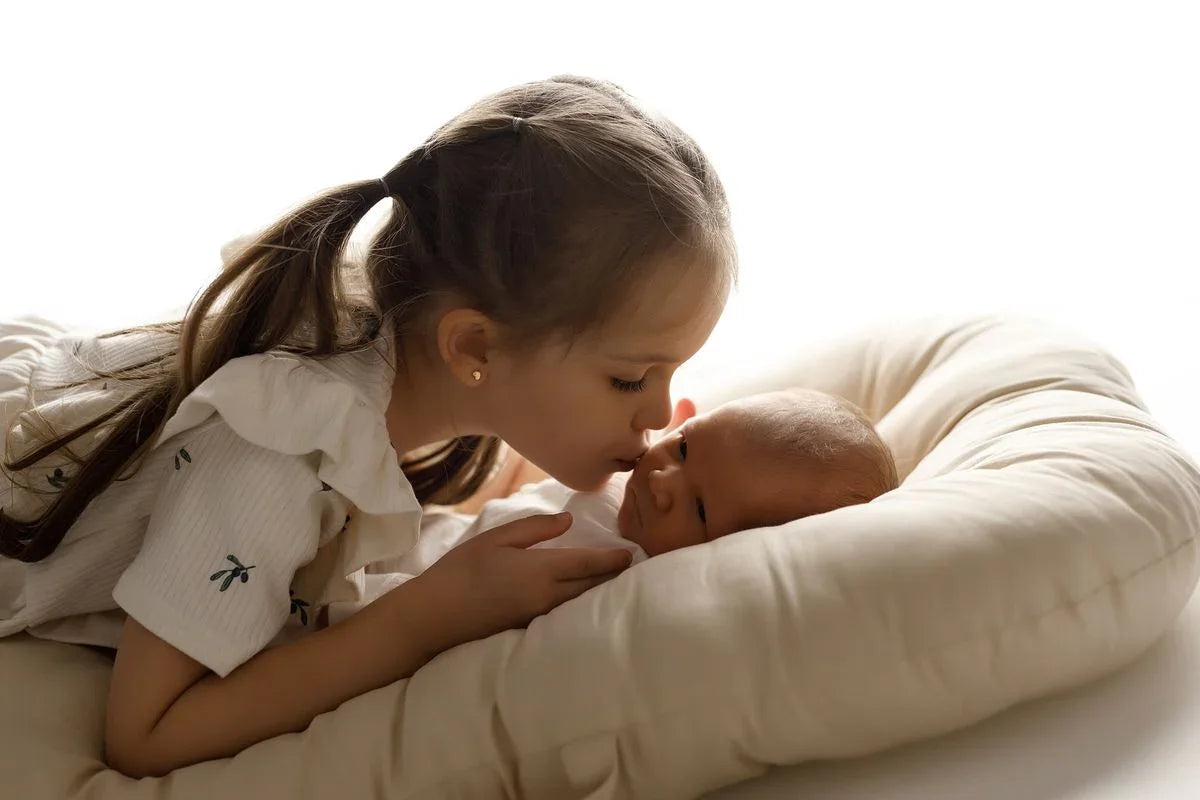 Petite fille embrassant un nouveau-né allongé dans un coussin de maternité, ambiance douce