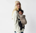 Femme portant un porte-bébé ergonomique en tissu beige avec un bébé souriant